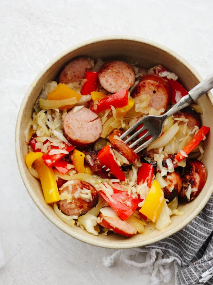 and flavored kielbasa layered in a bed of savory sauerkraut, this is a meal that your entire family will love! It's packed full of veggies and it's ready to eat in less than 30 minutes! The top view of a bowl filled with kielbasa and sauerkraut and a fork getting a bite.