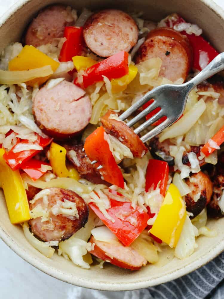 and flavored kielbasa layered in a bed of savory sauerkraut, this is a meal that your entire family will love! It's packed full of veggies and it's ready to eat in less than 30 minutes! Kielbasa and Sauerkraut in a bowl with a fork.