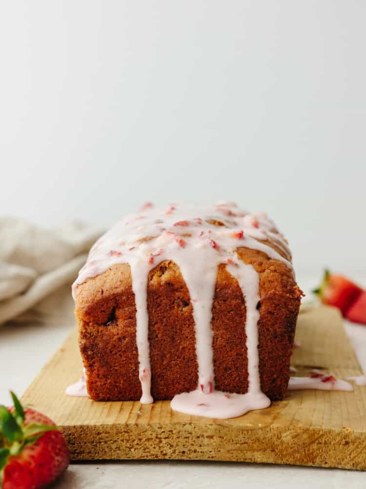 This strawberry quick bread is one of my all-time favorites! It is moist, packed with flavor, and drizzled with the most delightful strawberry glaze, which really brings all of the ingredients together. A loaf of strawberry bread on a wooden cutting board with strawberry glae dripping off the top.