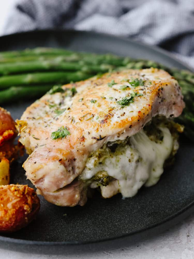 These cheesy stuffed pork chops are juicy and tender and baked to perfection! These not only make any dinner look fancy but they also taste amazing! A close up shot of a post chop on a plate stuffed with cheese and pesto sauce.
