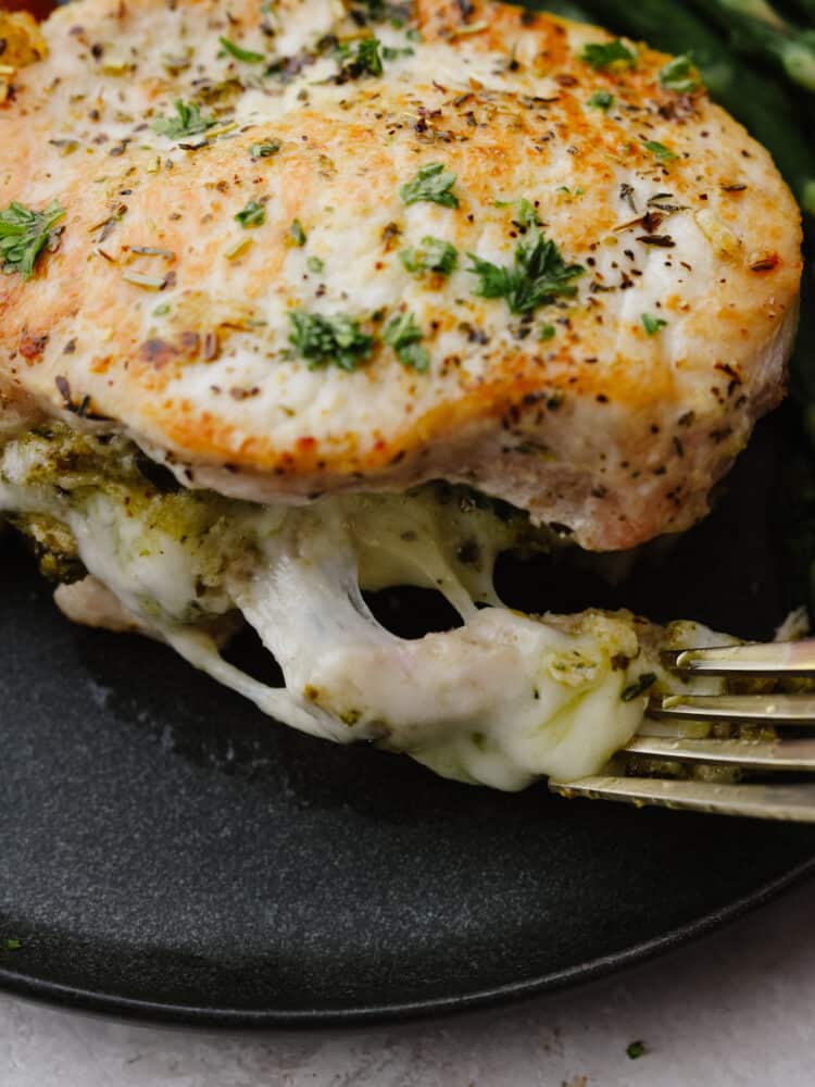 These cheesy stuffed pork chops are juicy and tender and baked to perfection! These not only make any dinner look fancy but they also taste amazing! A close up shot of a fork cutting into a stuffed pork chop.