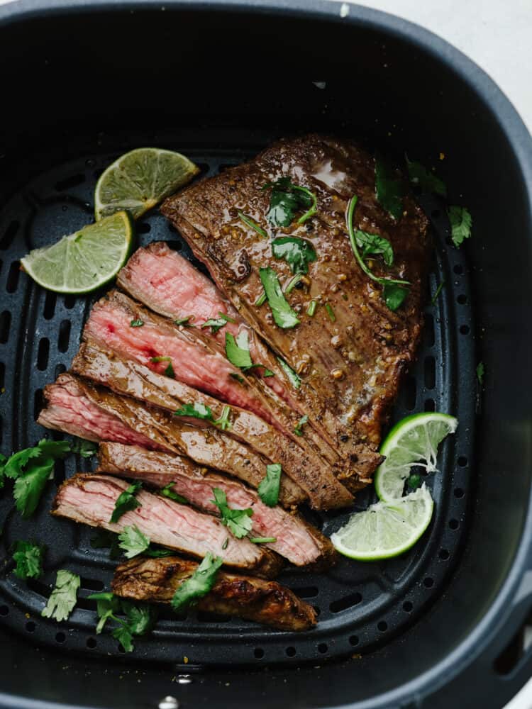 No more firing up the grill to enjoy juicy and tender steak. This flavorful flank steak comes together quickly after it is marinated and air-fried to perfection! Cooked and sliced flank steak, garnished with lime, in the basket of an air fryer.