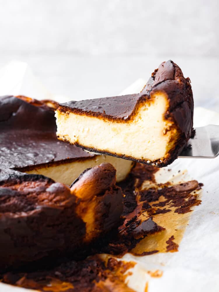 Try not to judge Basque cheesecake by its burnt outer layer because it's meant to be caramelized to perfection. You will be blown away by the rich and creamy Inside of this unique cheesecake. Side view of a slice of cheesecake being lifted away from the cheesecake.
