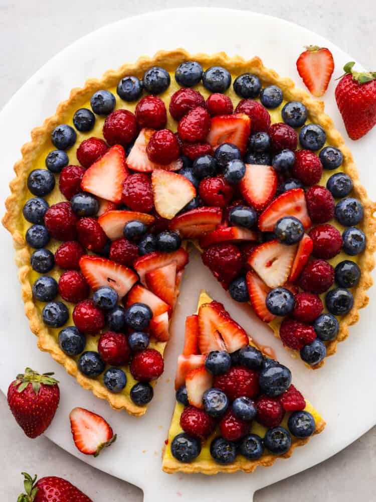 A buttery, flaky homemade crust, vanilla bean custard filling, and juicy berries make this berry tart the ultimate summer dessert! It's a beautiful and delicious way to showcase all the best fruit this season has to offer! Top-down view of a berry tart with a slice taken out of it.