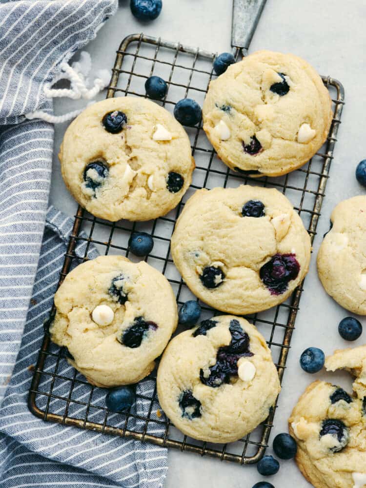 These blueberry cookies are packed with plump blueberries, white chocolate, and zesty lemon for an irresistible flavor combination! Bright, juicy, and sweet, this is one summer cookie recipe you wonโt want to miss. Top-down view of 5 cookies on a cooling rack.