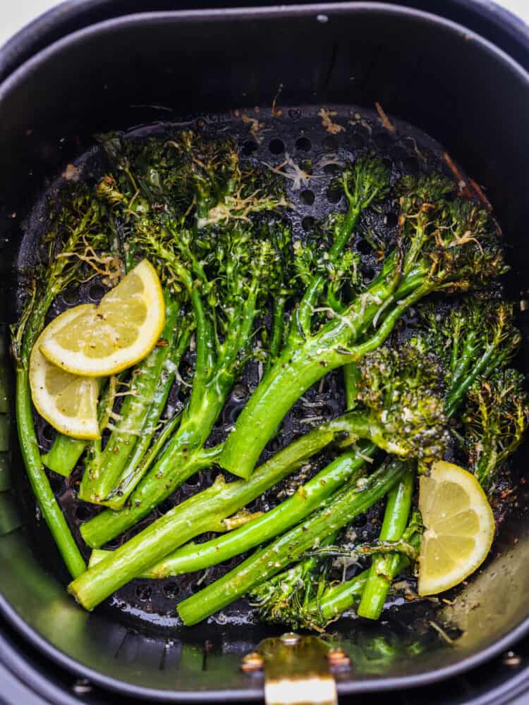 This super-easy side dish is delicious, full of flavor, and has the perfect crispy crunch on the outside. This air fryer broccolini takes less than 10 minutes to make and can be paired with just about any meal! An air fryer basket with cooked broccolini and some lemon slices.