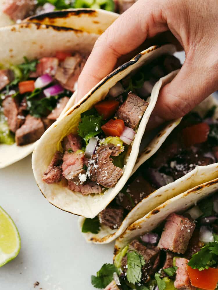 Carne asada tacos are a go-to recipe in our family! You can fill the tortilla to the brim with all of your favorite toppings, and everyone (even picky eaters!) will go crazy over this meal! A carne asada taco folded in half and being held.
