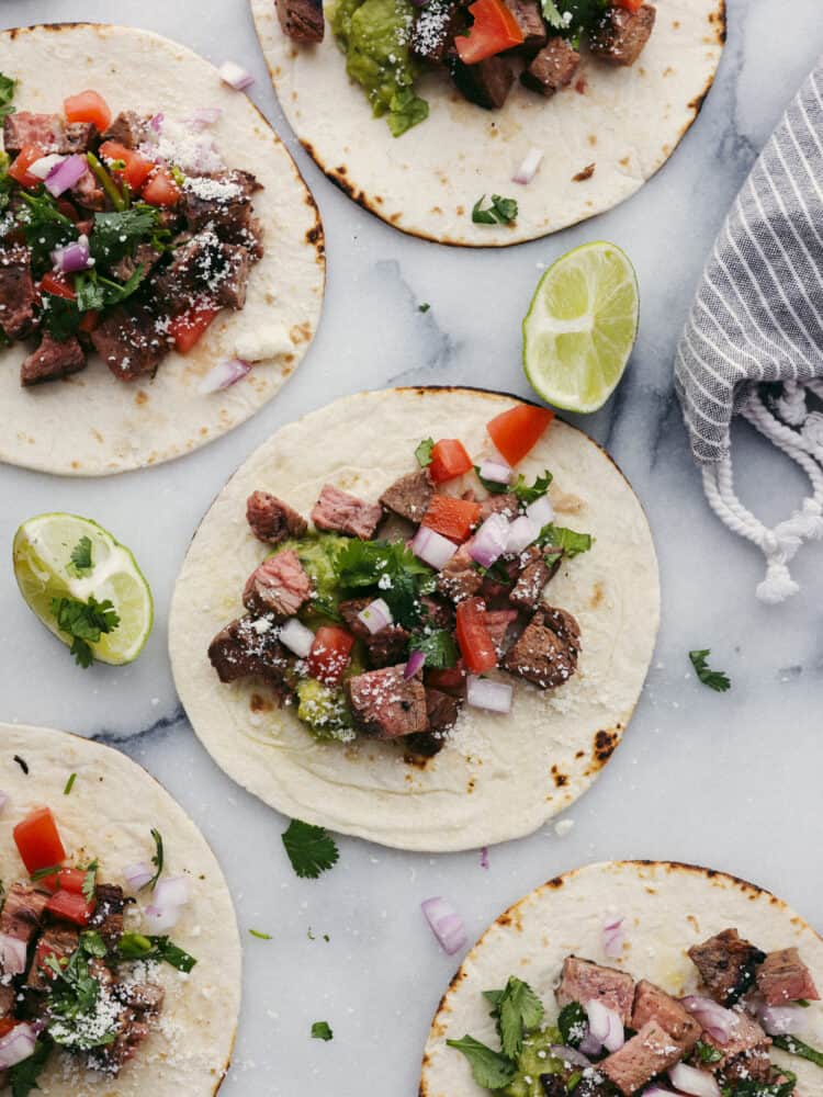 Carne asada tacos are a go-to recipe in our family! You can fill the tortilla to the brim with all of your favorite toppings, and everyone (even picky eaters!) will go crazy over this meal! Tortillas laying flat that have toppings on them.
