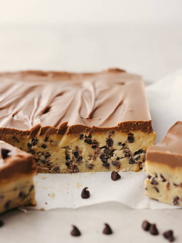 Get ready for these chocolate chip cookie dough bars to become a favorite you makeย all the time!ย Perfectly creamy and delicious (and with no raw egg), these bars will get devoured by anyone lucky enough to eat them! The side view of the chocolate chip cookie dough on parchment paper, ready to be cut.