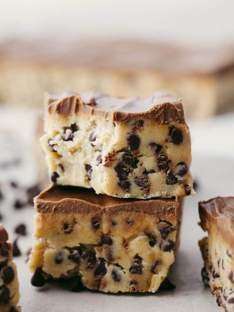 Get ready for these chocolate chip cookie dough bars to become a favorite you makeย all the time!ย Perfectly creamy and delicious (and with no raw egg), these bars will get devoured by anyone lucky enough to eat them! A stack of cookie dough bars, the top one has a bit taken out of it.