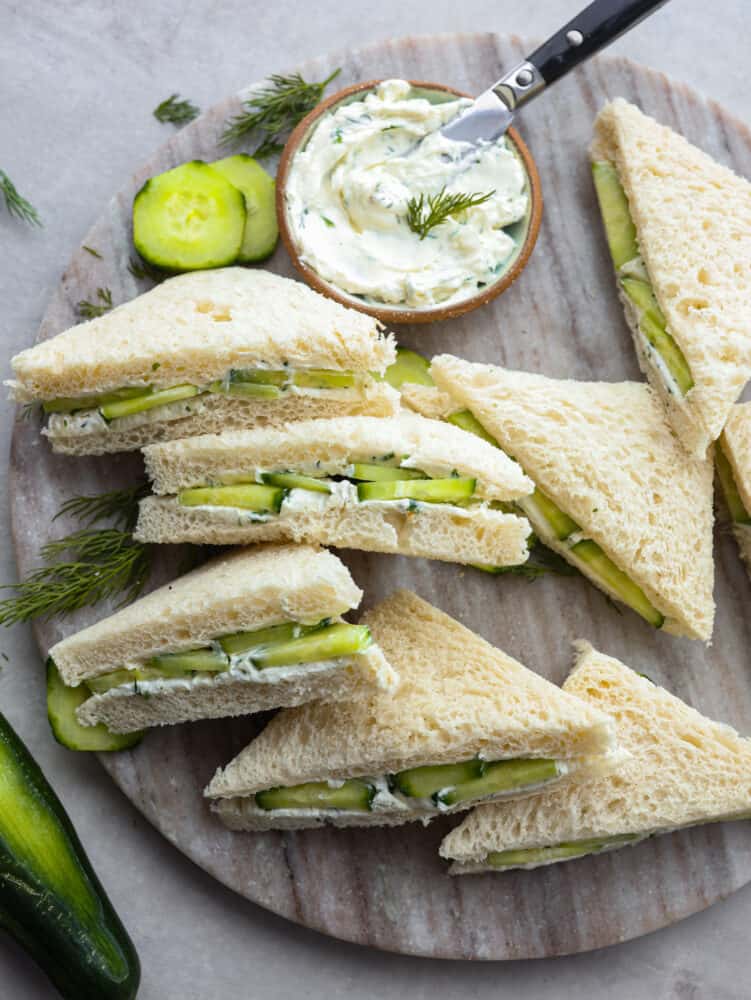 Cool and crisp, cucumber sandwiches are the perfect summer appetizer! Each sandwich is lined with a creamy lemon herb spread for a pop of zesty flavor. You'll love them! Top-down view of sliced cucumber sandwiches served with lemon dill spread.