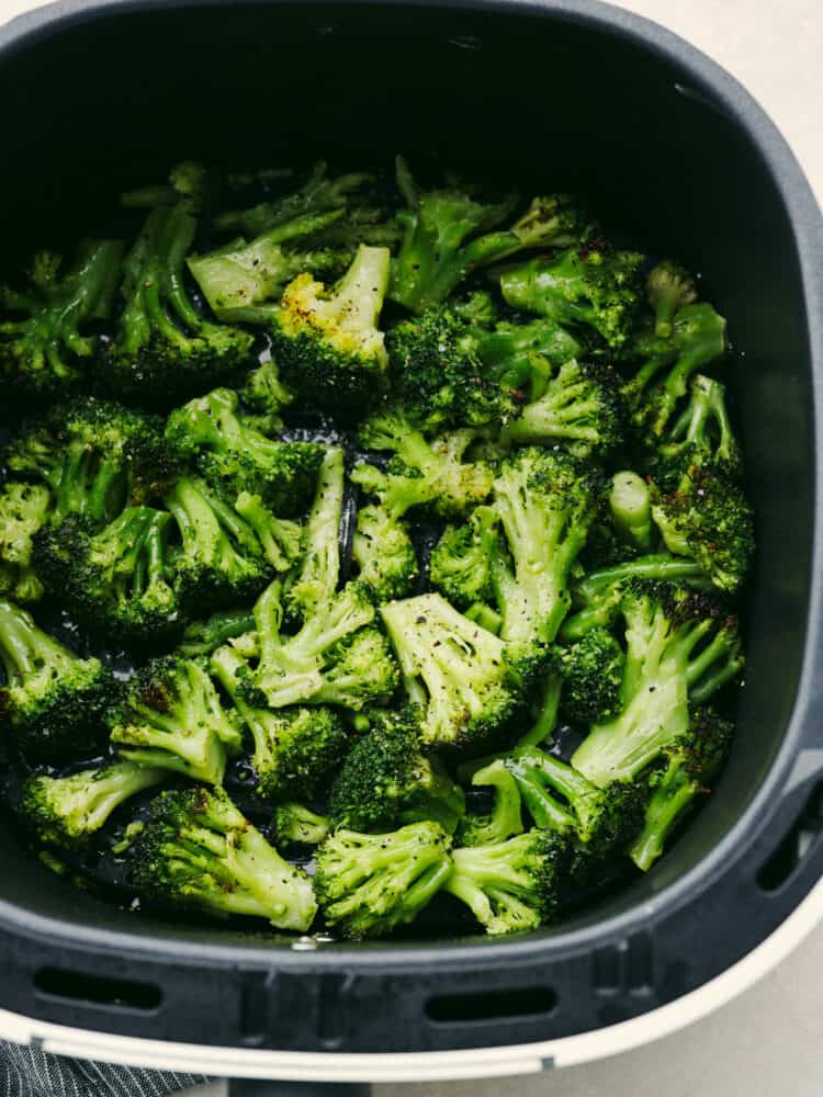 Air fryer frozen broccoli is so easy and delicious! Whip up that classic roasted broccoli texture and flavor with no mess (and in under 10 minutes!) so that it can go with any meal! Broccoli in an air fryer basket seasoned with salt and pepper.