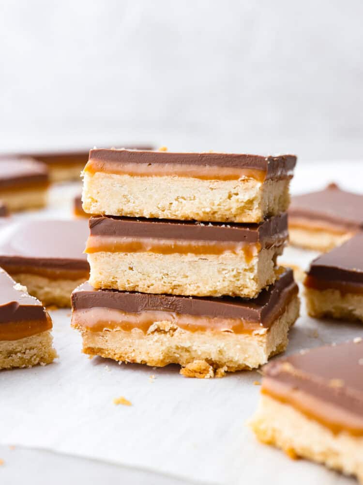 These taste exactly like a Twix bar with a delicious shortbread crust, caramel center, and a chocolate layer on top. The best part about them is that you can make them right at home! A stack of homemade twix bars.