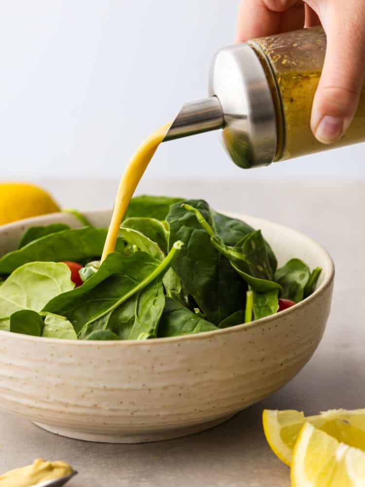 Homemade honey mustard dressing will give any salad the best boost of sweet and tangy flavor. You only need a handful of simple ingredients to whip it up. Once you've made it yourself, you won't want it any other way! Pouring honey mustard dressing over a green salad in a stoneware bowl.