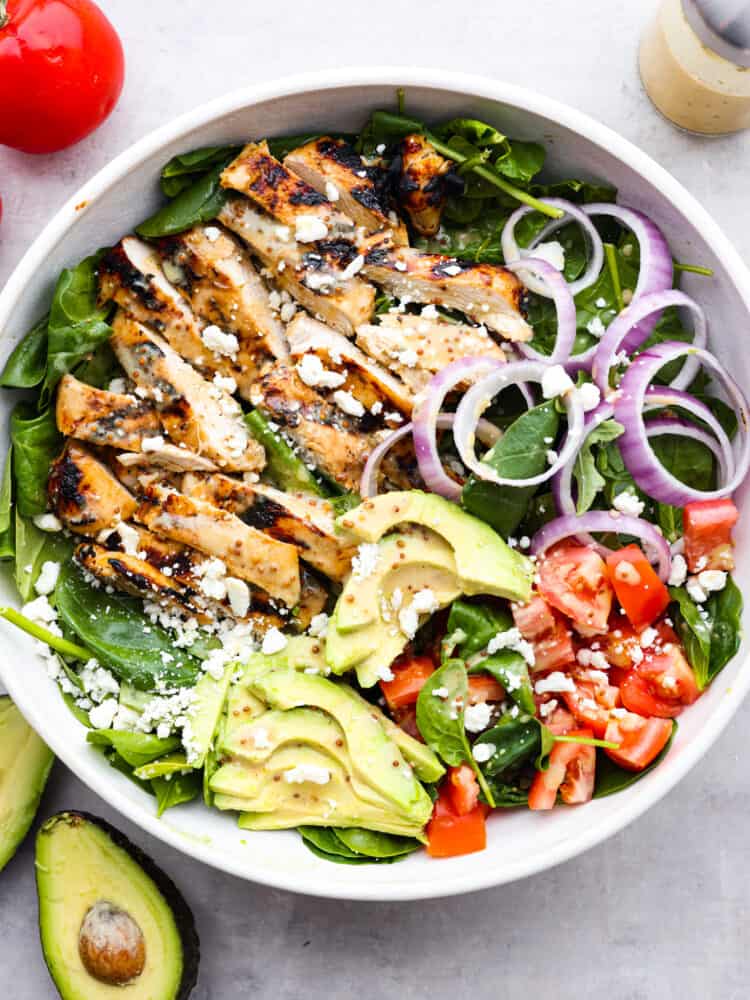 This honey mustard chicken salad is easy to put together and is bursting with flavor. Plus, it's hearty enough to be a complete meal for dinner and leave you fully satisfied. The top view of a honey mustard chicken salad with avocado, spinach, tomatoes, red onions and feta cheese.