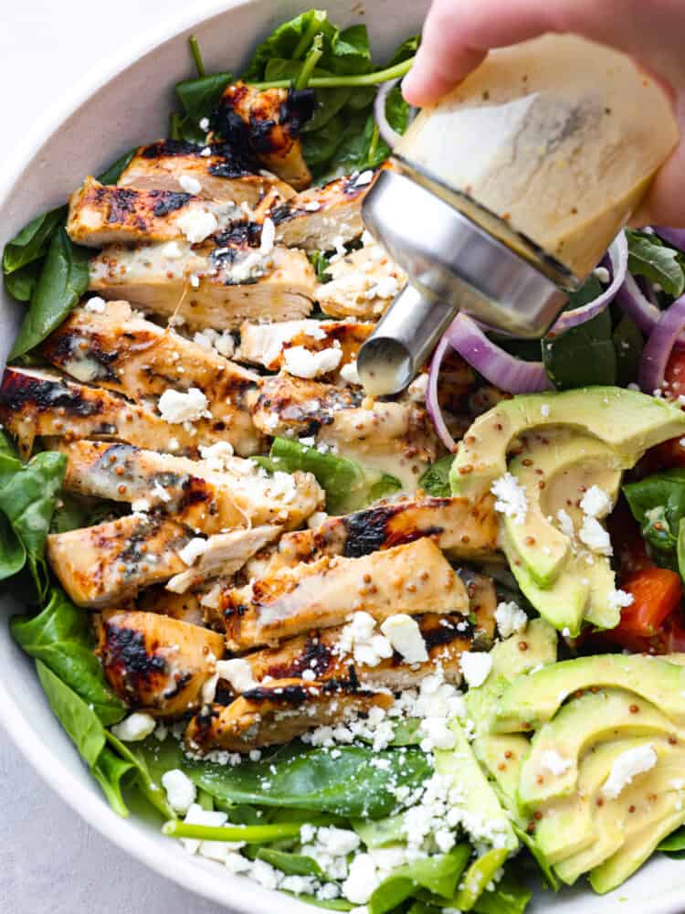 This honey mustard chicken salad is easy to put together and is bursting with flavor. Plus, it's hearty enough to be a complete meal for dinner and leave you fully satisfied. Honey mustard salad dressing being poured onto a salad.