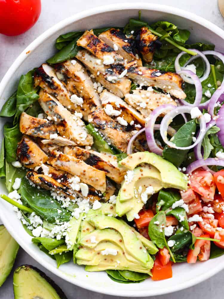 This honey mustard chicken salad is easy to put together and is bursting with flavor. Plus, it's hearty enough to be a complete meal for dinner and leave you fully satisfied. A salad bowl with spinach, avocado, honey mustard chicken, tomatoes, onions and feta cheese.