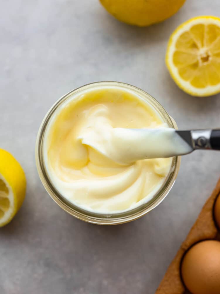 Easy homemade mayonnaise is fresh and convenient to make right at home. With just a few ingredients, you can make this delicious and versatile condiment to use on sandwiches or in dips and sauces! Top view photo of mayonnaise in mason jar with a knife covered in mayonnaise and lifting out of the jar.