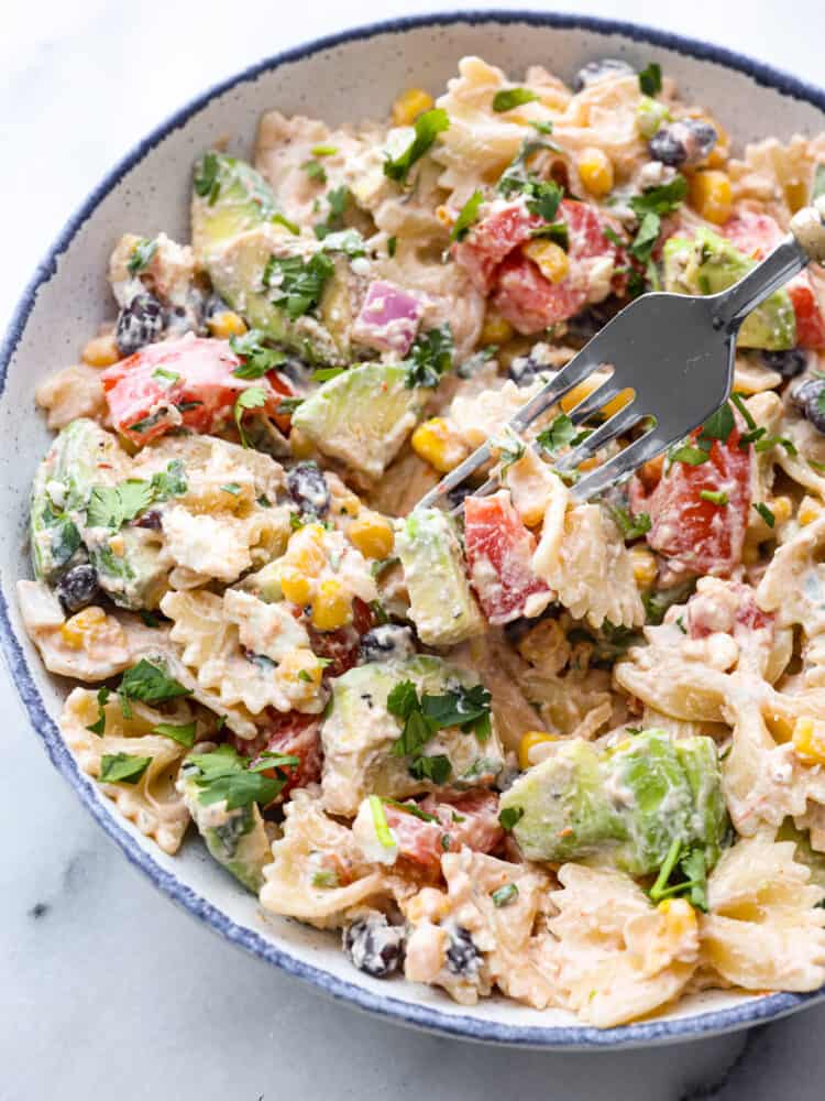 Mexican Pasta Salad is an unbelievably easy and flavorful pasta salad that is filled with colorful ingredients like black beans, tomatoes, and corn.ย With a creamy dressing and spices from onion, cilantro, and cumin, this delicious pasta salad will be the hit of your summer barbecues for sure! Mexican pasta salad in a bowl with a fork.