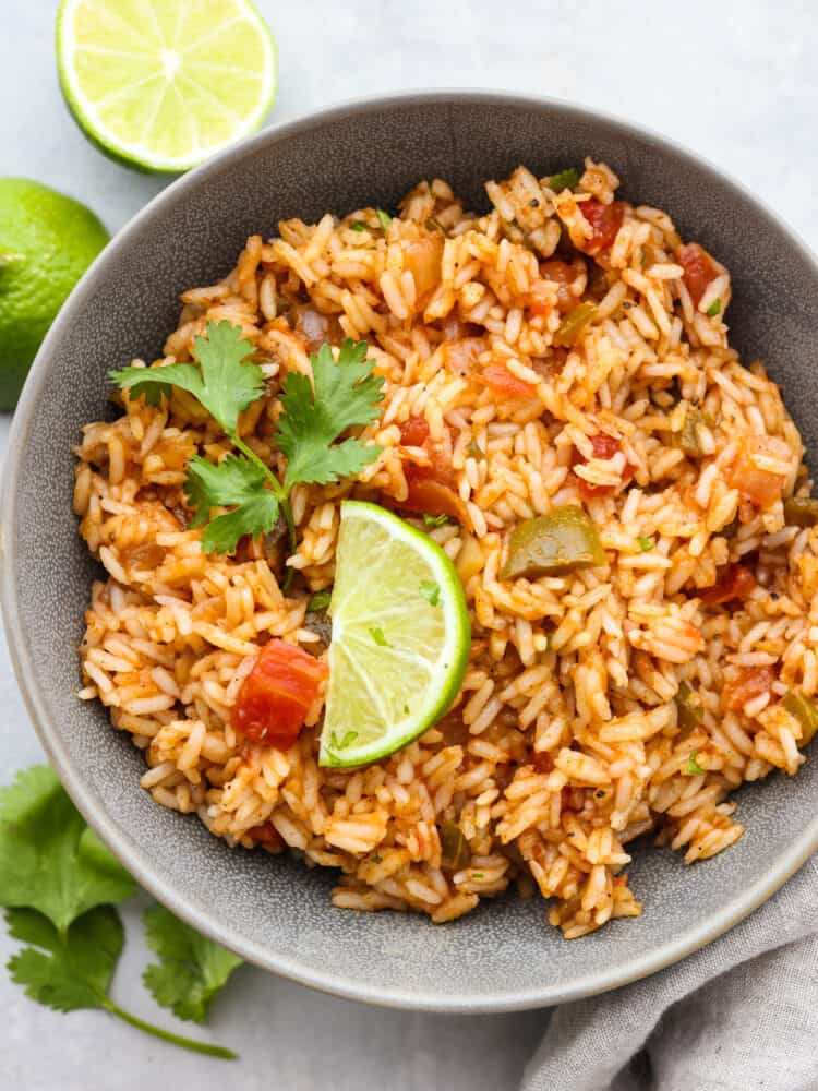 This Mexican Rice is so easy to make! Simmered until tender in broth, salsa and a mix of spices gives it a ton of flavor, perfect for adding to any fiesta. #mexican #rice #dinner A bowl of Mexican rice garnished with cilantro and a slice of lime.