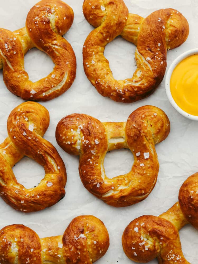 Disney fans, these pretzels are for you! They are golden brown on the outside, have a soft texture on the inside, and are topped with coarse salt. And, they are shaped like Mickey! A soft pretzel doesn't get much better than that! The top voew of cooked Mickey pretzels on parchement paper. There is a small bowl of cheese sauce on the side.