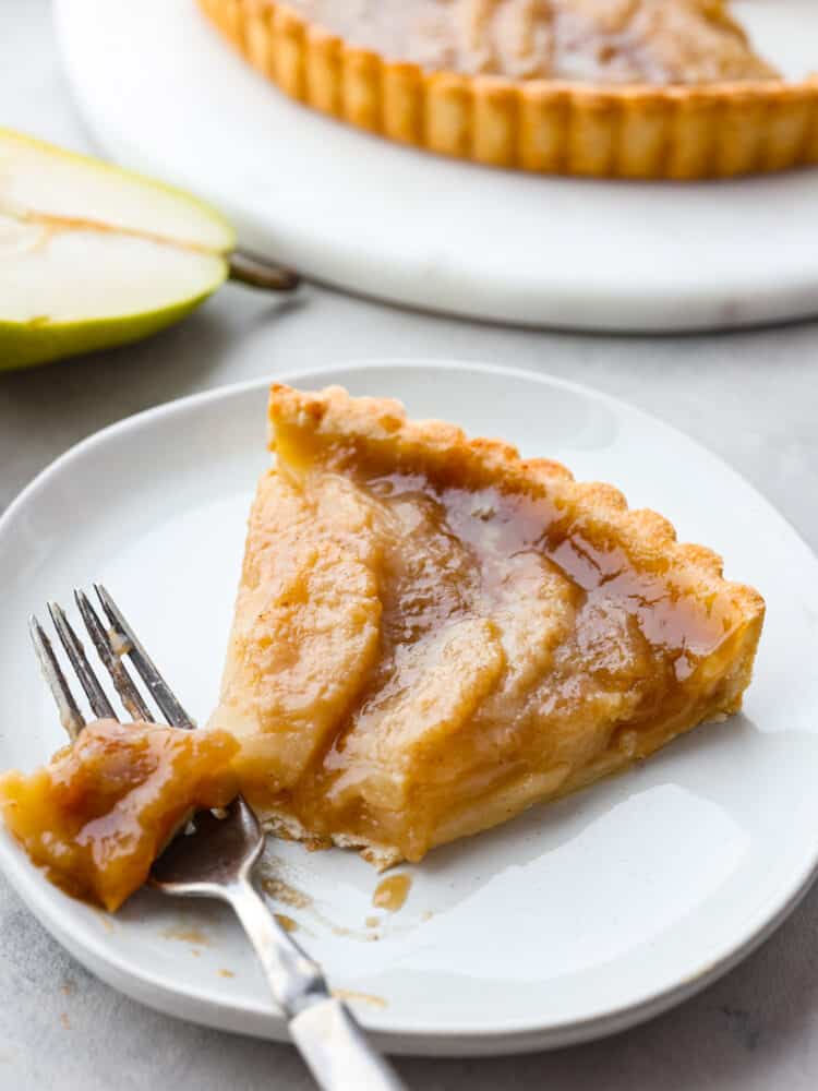 This pear tart is as delicious as it is gorgeous! It has a perfectly flaky crust topped with sliced pears and covered with a delightful brown sugar crumb topping. A slice of pear tart on a plate with a silver fork cutting a piece of it.