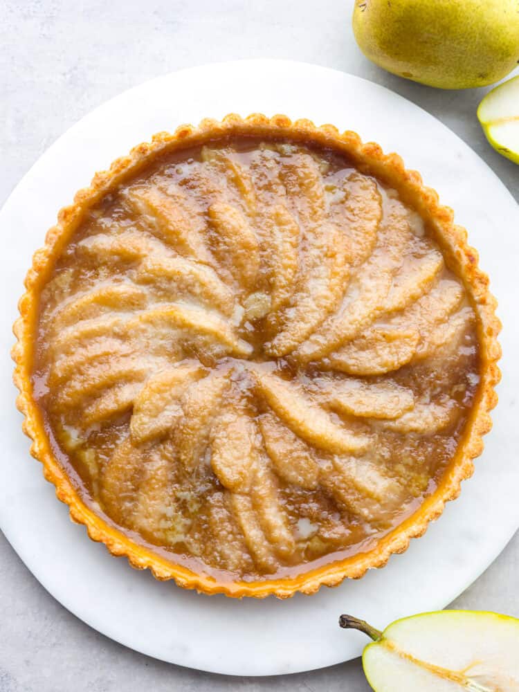 This pear tart is as delicious as it is gorgeous! It has a perfectly flaky crust topped with sliced pears and covered with a delightful brown sugar crumb topping. The top view of a pear tart on a white platter.