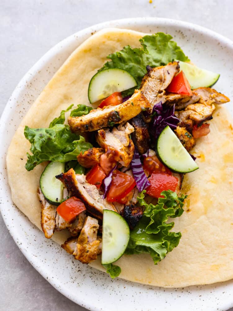 This Middle Eastern chicken shawarma is packed full of flavorful chicken that is seasoned with a delightful array of spices. It makes a great lunch or dinner that everyone will go crazy for! A pita on a plate topped with veggies and chicken shawarma.
