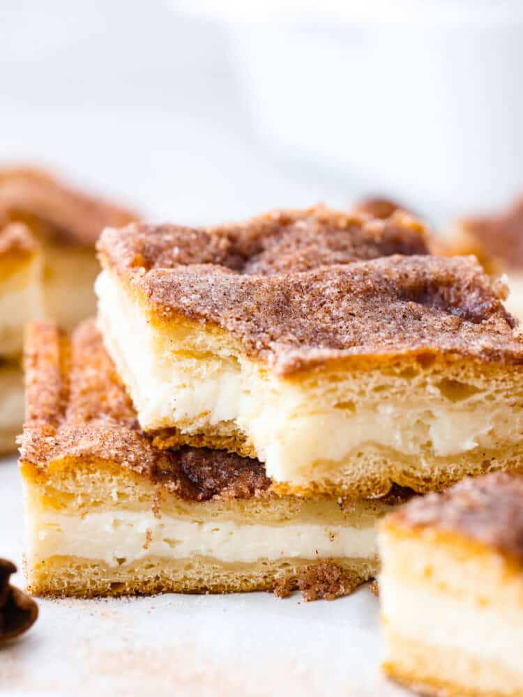 These sopapilla cheesecake bars have the most delicious flakey, cinnamon sugar crust on the top and the bottom. Sandwiched in between is a creamy cheesecake filling that everyone will go crazy over! 2 sopapilla bars stacked on one another. The top one has a bite taken out of it.
