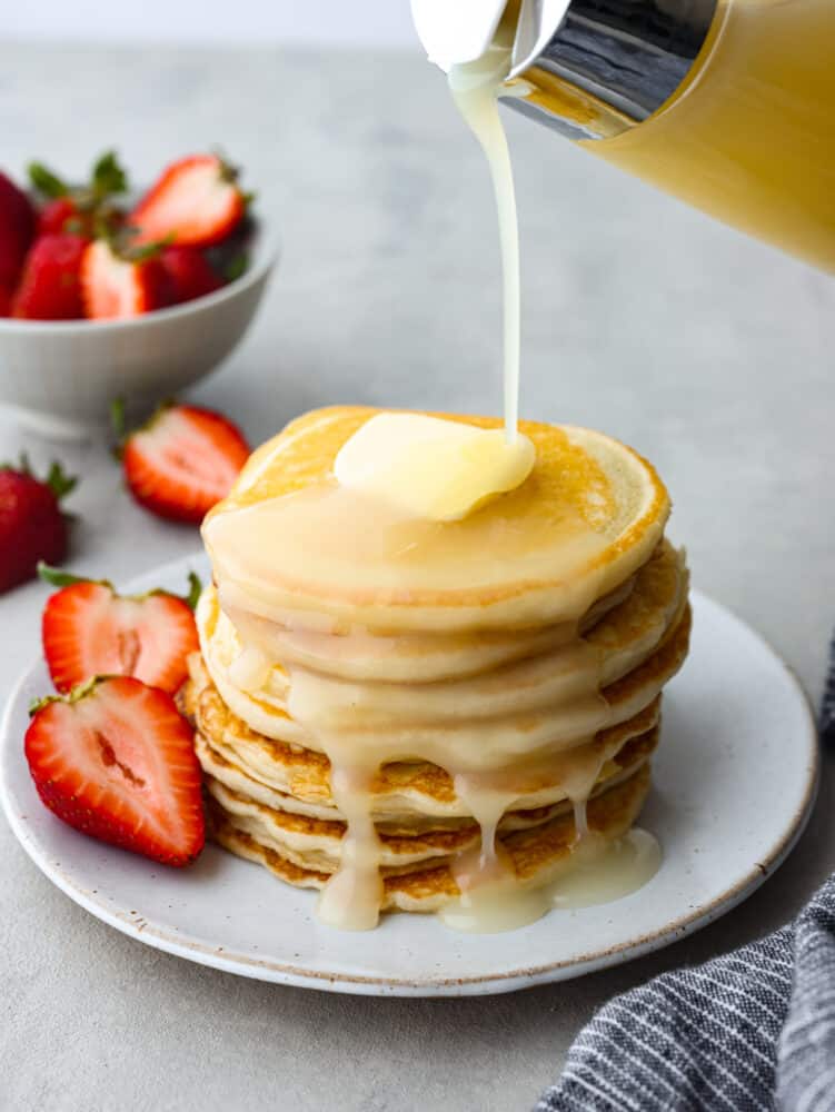 These sour cream pancakes are perfectly fluffy and soft. Their delightful taste pairs perfectly with any syrup that you love and your entire family will go crazy over these! A stack of sour cream pancakes with coconut syrup being poured on them.