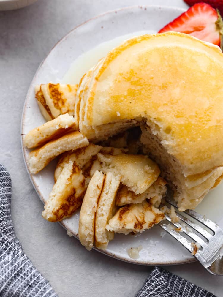 These sour cream pancakes are perfectly fluffy and soft. Their delightful taste pairs perfectly with any syrup that you love and your entire family will go crazy over these! The top view of a stack of pancakes with a piece cut out with a fork.