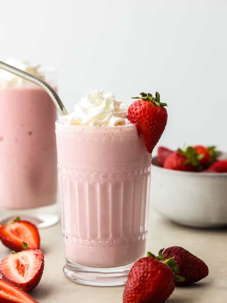 This strawberry milkshake is thick, creamy, and everything that you would hope a milkshake would be! Made with delicious strawberries, this classic dessert is sure to be loved by all! A strawberry milkshake in a glass with a silver straw and a fresh strawberries on the side.