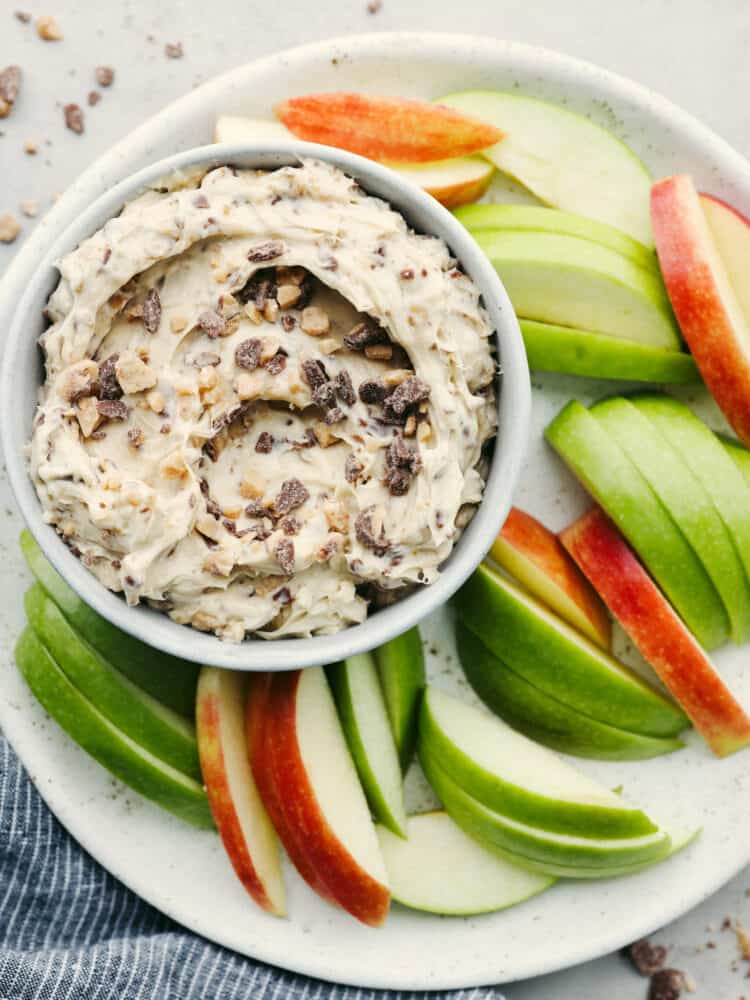 Toffee apple dip is a family favorite! A sweet dip complete with heath bar candy bits and cream cheese mixed with brown sugar, this dip is so delicious you won't be able to stop eating it! Dip in a bowl on a platter filled with apple slices.
