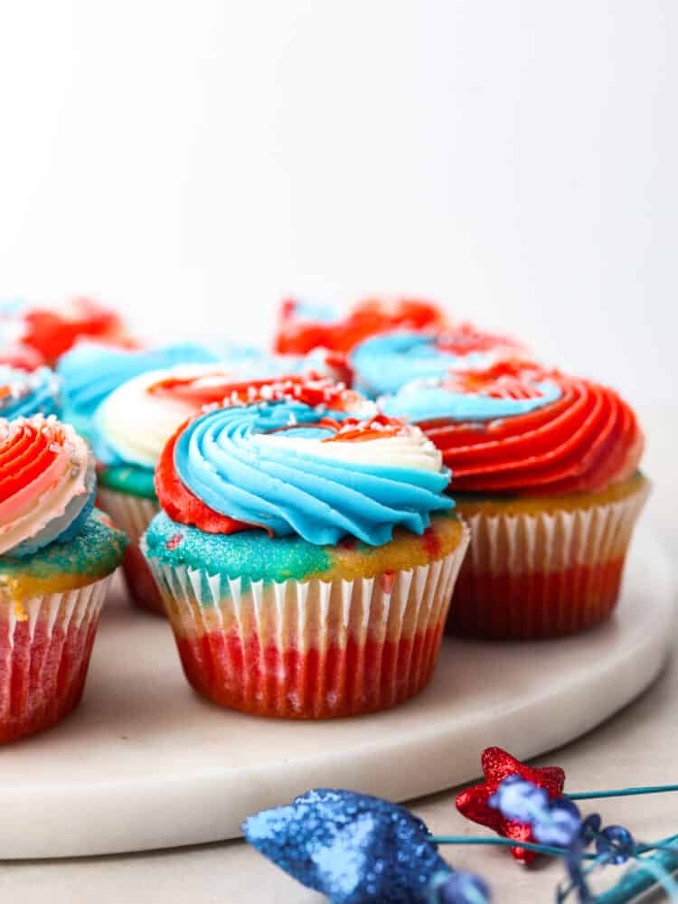 These festive red, white and blue cupcakes are perfect for celebrating the 4th of July this year! They are tender, moist, and swirled with all the colors perfect for celebrating! Red, white and blue cupcakes on a marble cutting board.