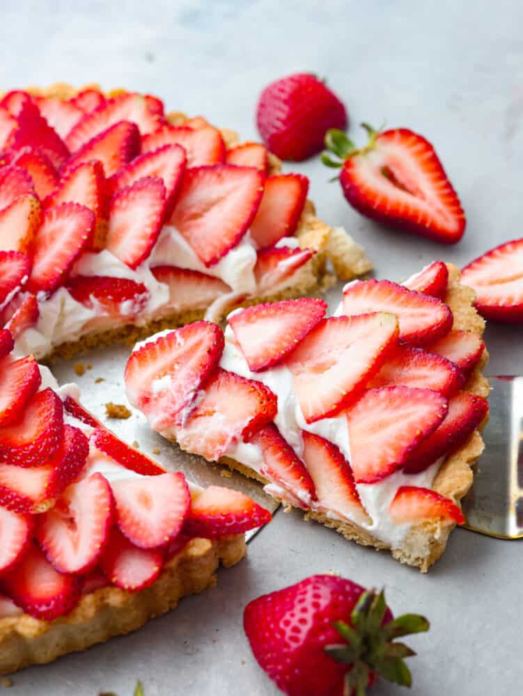 A perfectly summery strawberry tart made with a buttery crust, smooth cream cheese-based filling, and fresh summer berries! Each bite is filled with creamy, juicy flavor that you won't be able to get enough of! A slice of tart being served with a cake spatula.