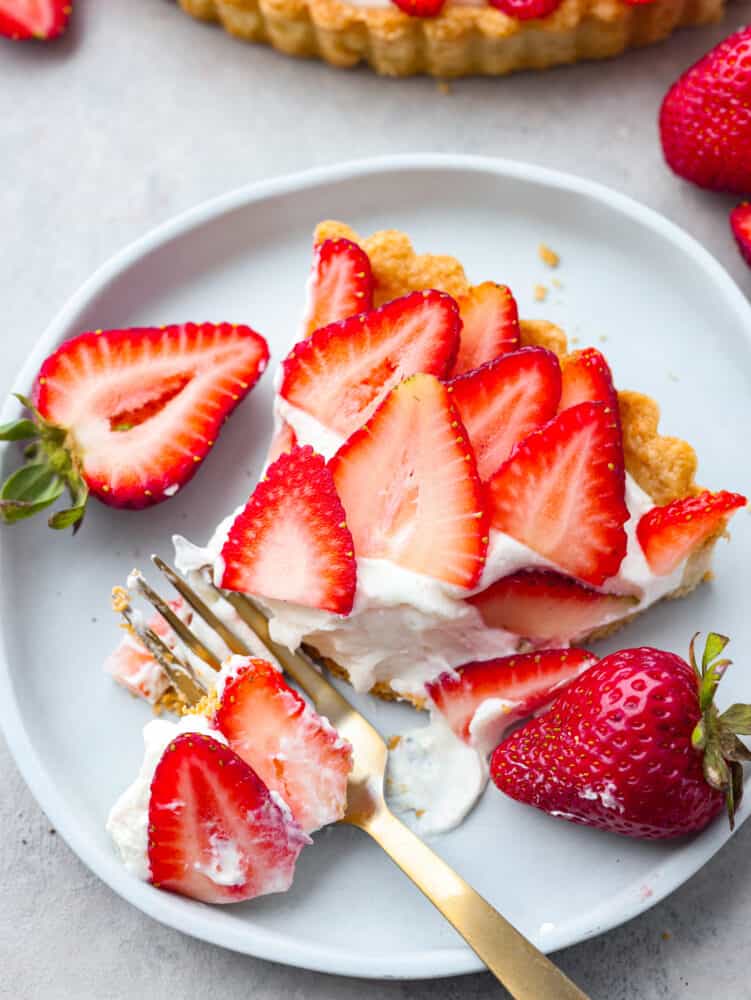 A perfectly summery strawberry tart made with a buttery crust, smooth cream cheese-based filling, and fresh summer berries! Each bite is filled with creamy, juicy flavor that you won't be able to get enough of! Taking a bite of strawberry tart with a gold fork.