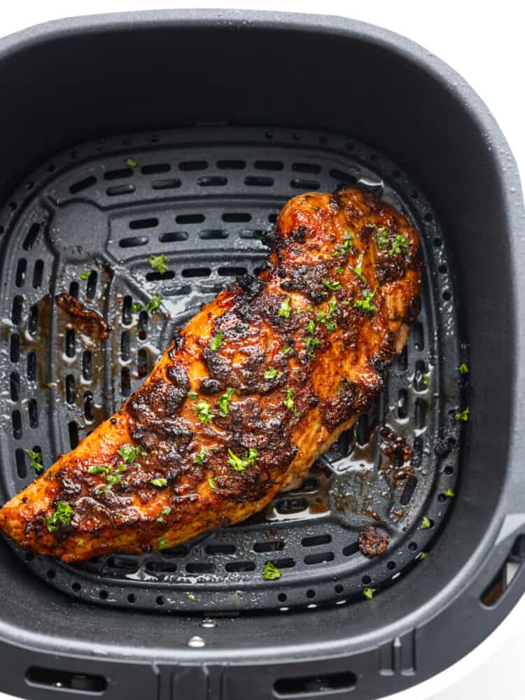 Air fryer pork tenderloin is the ultimate weeknight dinner hero! It's quick, juicy, and packed with flavor! It cooks up perfectly with minimal effort, thanks to a simple marinade and the magic of the air fryer. Top view of finished cooked pork tenderloin in the air fryer basket and garnished with fresh parsley.