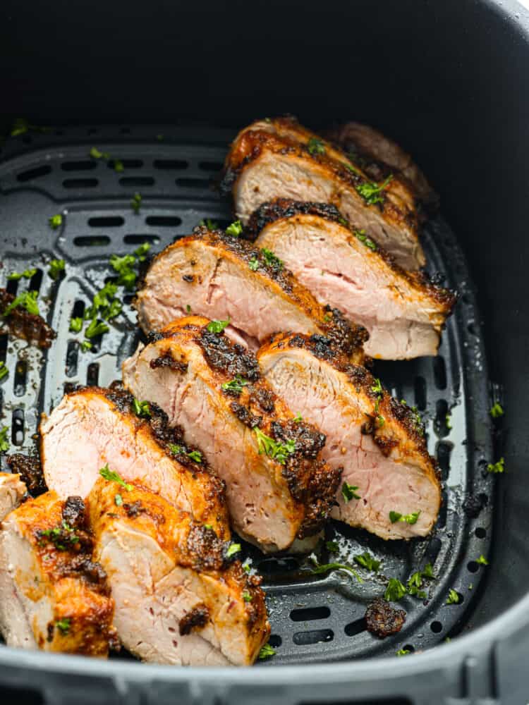 Air fryer pork tenderloin is the ultimate weeknight dinner hero! It's quick, juicy, and packed with flavor! It cooks up perfectly with minimal effort, thanks to a simple marinade and the magic of the air fryer. Top view of cooked sliced pork tenderloin in the air fryer. Garnished with fresh parsley.