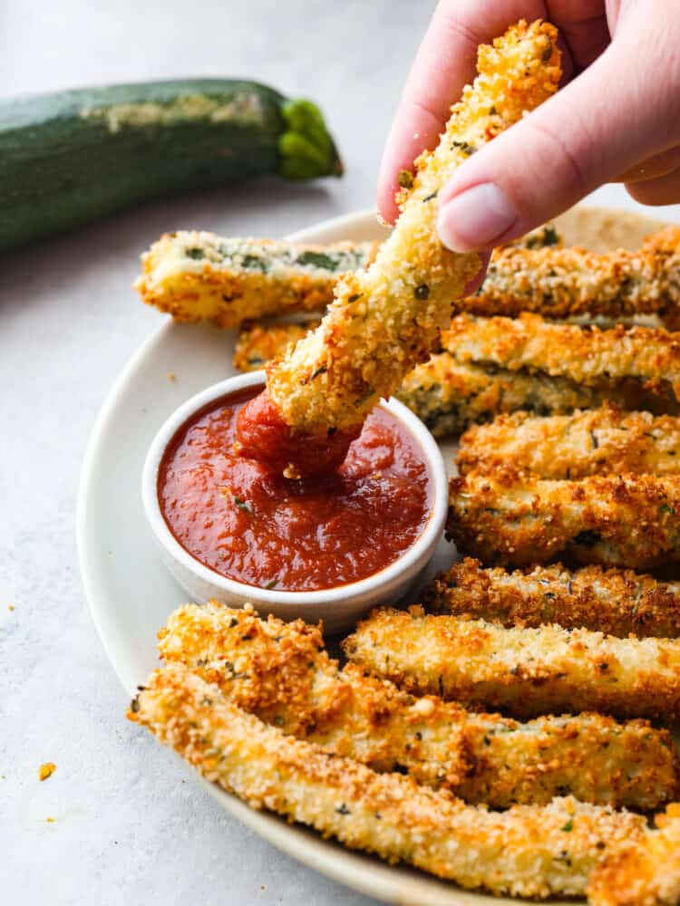 Air fryer zucchini fries are a low-carb, keto-friendly snack that's ready in minutes! Crispy and cheesy on the outside, tender on the inside, this is the best way to use up your leftover summer zucchini. Dipping a zucchini fry into marinara sauce.