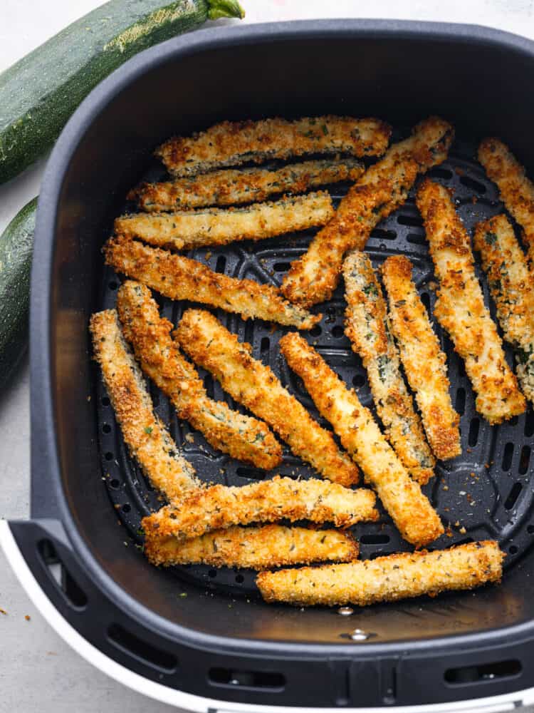 Air fryer zucchini fries are a low-carb, keto-friendly snack that's ready in minutes! Crispy and cheesy on the outside, tender on the inside, this is the best way to use up your leftover summer zucchini. Cooked zucchini fries in the bottom of an air fryer basket.