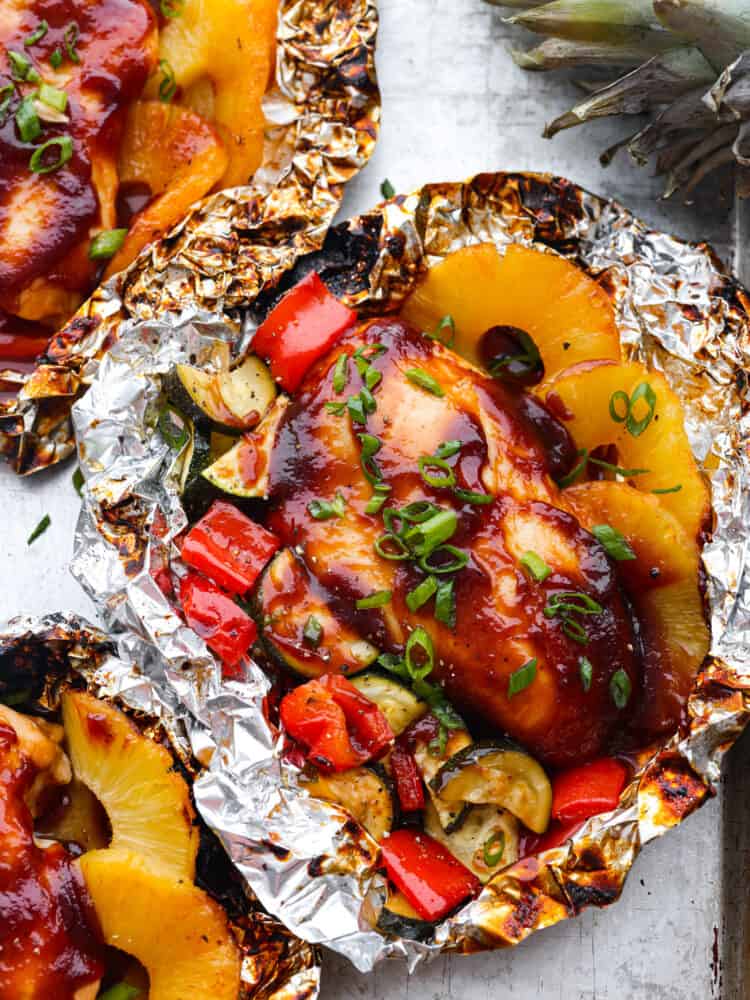 Grilled Hawaiian barbecue chicken in foil has the most amazing sweet and tangy pineapple barbecue sauce! It grills to perfection with fresh pineapple and delicious summer veggies! Cooked BBQ chicken in aluminum foil surrounded by cooked pineapple and veggies.