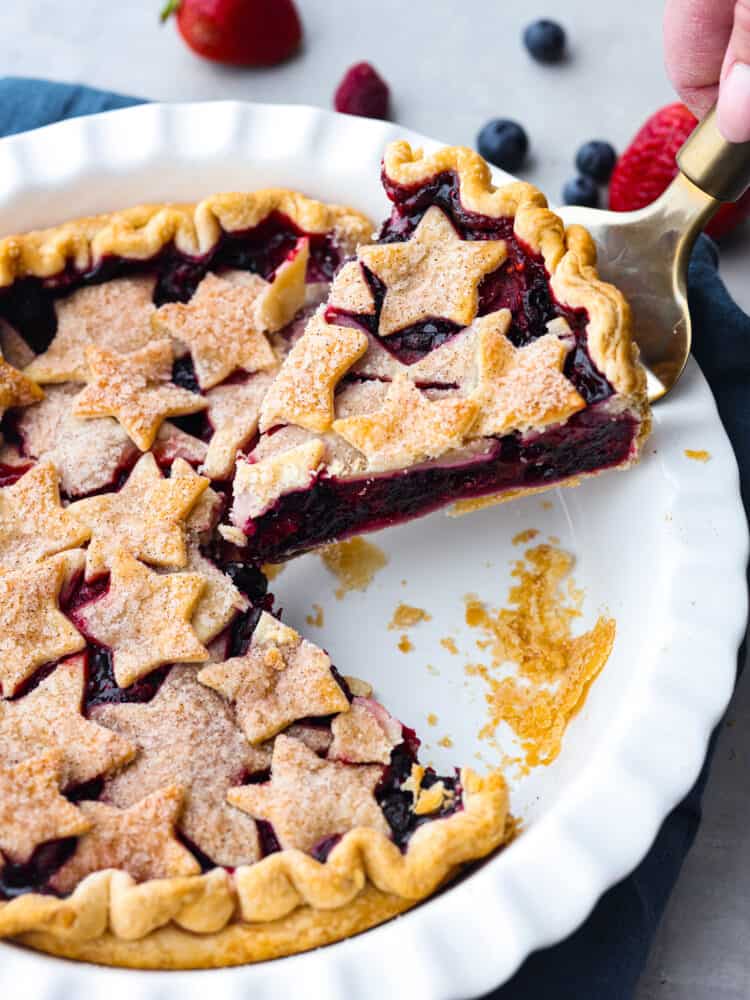 A patriotic fourth-of-July triple berry pie made simple with easy ingredients! This berry pie is bursting with juicy flavor and almost looks too good to eat. It's the perfect centerpiece for any summer celebration! Picking up a slice of pie with a cake spatula.