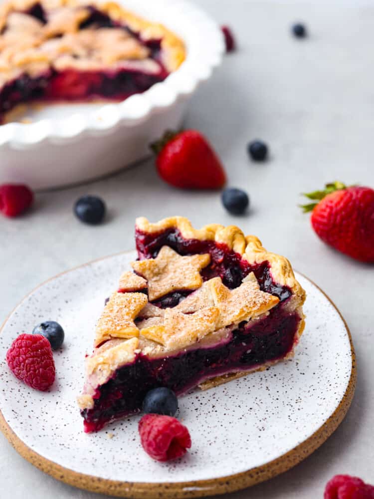 A patriotic fourth-of-July triple berry pie made simple with easy ingredients! This berry pie is bursting with juicy flavor and almost looks too good to eat. It's the perfect centerpiece for any summer celebration! A slice of triple berry pie on a stoneware plate.