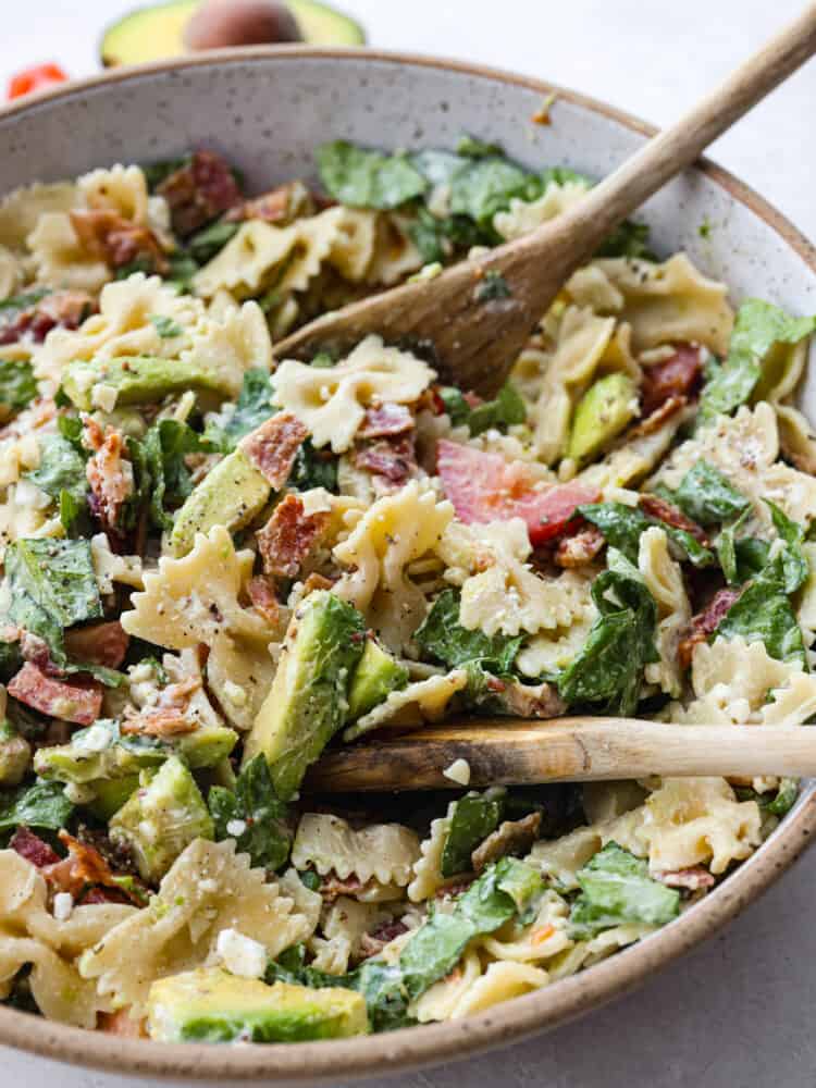 BLT avocado pasta salad is fresh and crisp romaine lettuce tossed in bacon, tomato, pasta, and avocado. Topped with a creamy dressing and sprinkled with feta cheese this is one amazing salad! A close up of BLT Avocado Pasta Salad with a wooden spoon.