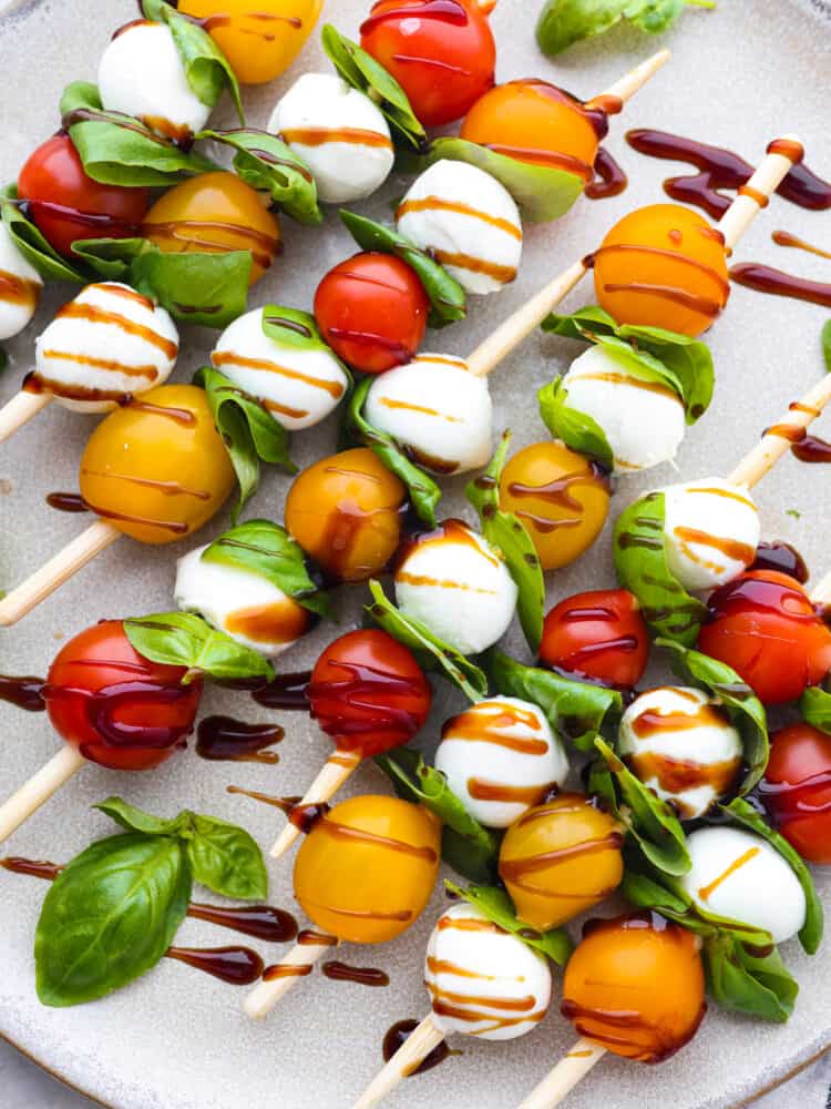 Caprese skewers are a 4-ingredient appetizer that is so simple but guaranteed to impress! Made with cherry tomatoes, mozzarella, fresh basil, and an easy balsamic reduction, they imitate classic Caprese salad, only made portable on a skewer! Caprese skewers drizzled with balsamic vinegar.