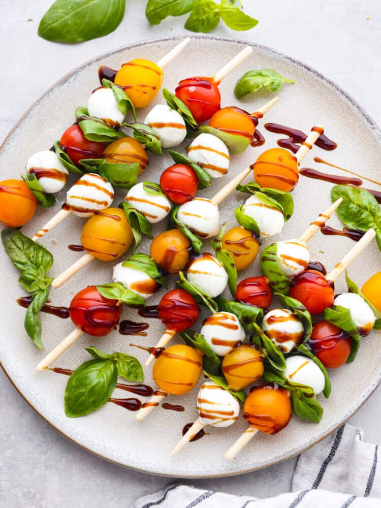 Caprese skewers are a 4-ingredient appetizer that is so simple but guaranteed to impress! Made with cherry tomatoes, mozzarella, fresh basil, and an easy balsamic reduction, they imitate classic Caprese salad, only made portable on a skewer! Top-down view of Caprese skewers on a gray plate.