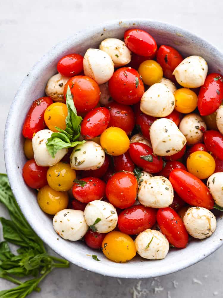 This cherry tomato salad is made with flavorful herbs, delicious cherry tomatoes, and fresh mozzarella! Coated in a delicious lemon basil dressing, this salad will soon be your new favorite! The top view of a bowl of cherry tomato salad.