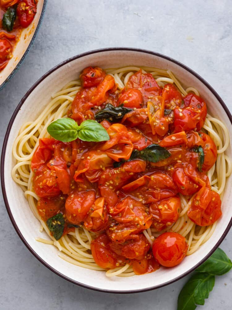 With just a few ingredients you can easily make tomato sauce using cherry tomatoes. Cherry tomatoes infused with fresh garlic and Italian seasonings make this cherry tomato sauce perfect for pasta, on top of roasted vegetables, or with a side of artisan bread. Overhead photo of pasta in a a white bowl with spaghetti noodles and cherry tomato sauce on top. Fresh basil garnished on top and on the side.