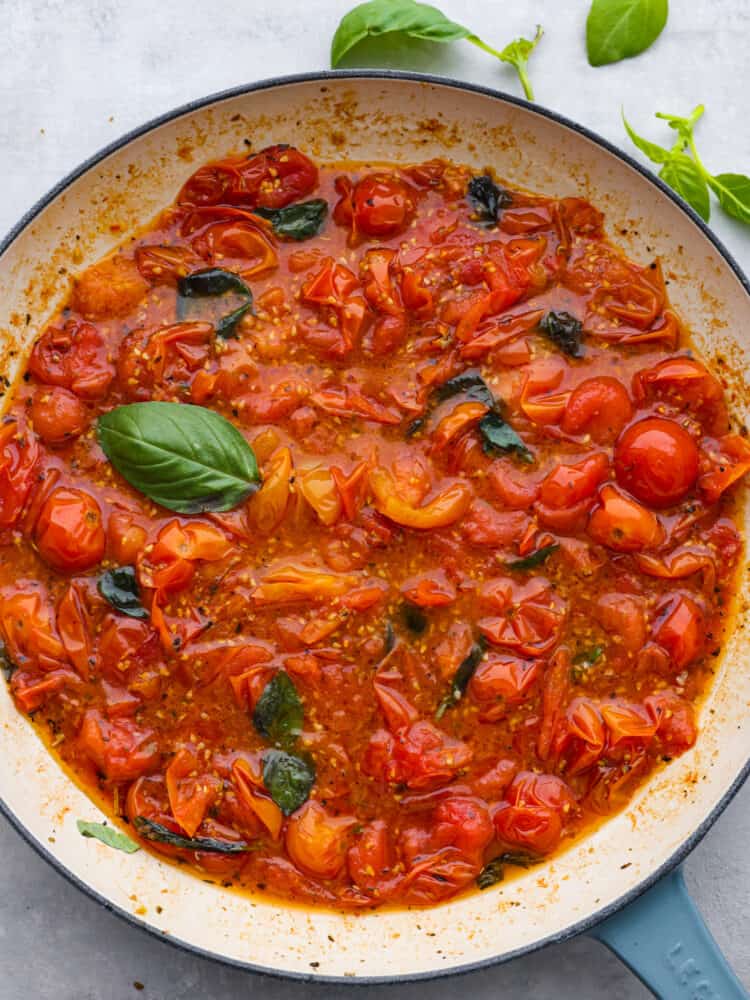 With just a few ingredients you can easily make tomato sauce using cherry tomatoes. Cherry tomatoes infused with fresh garlic and Italian seasonings make this cherry tomato sauce perfect for pasta, on top of roasted vegetables, or with a side of artisan bread. Overhead photo of cherry tomato sauce in a blue skillet with fresh basil on the side.