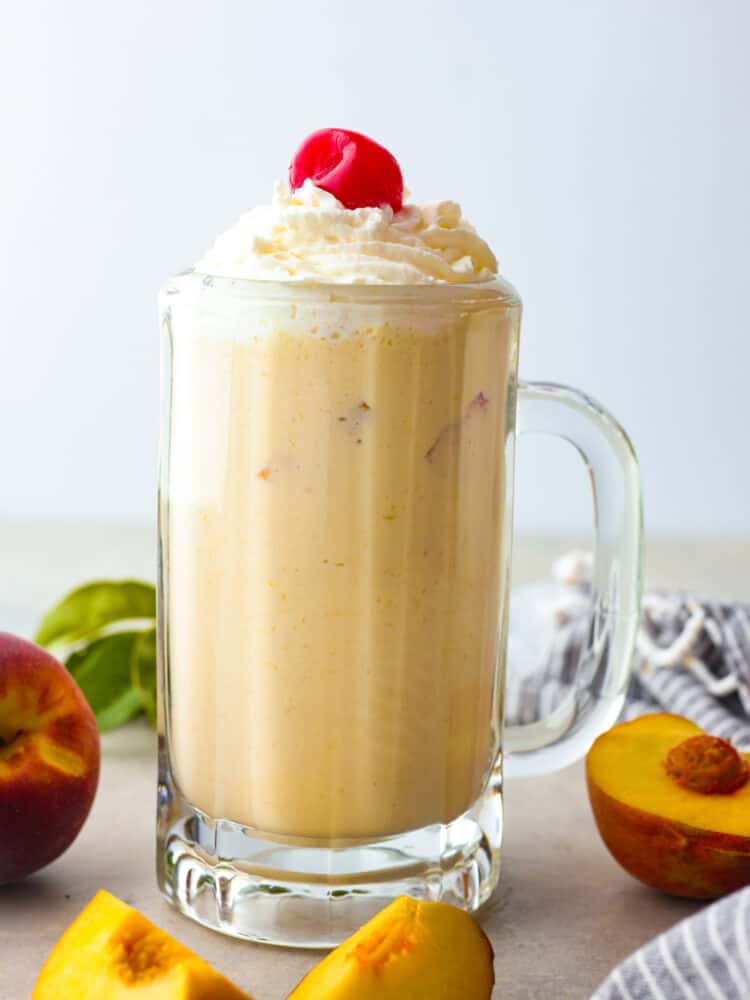 Chick-fil-A's peach shakes are the best summer treat! Now you can enjoy this delicious seasonal drink all year long with this quick and easy copycat recipe. It's too creamy and indulgent to pass up! A peach milkshake in a glass mug, garnished with a cherry.